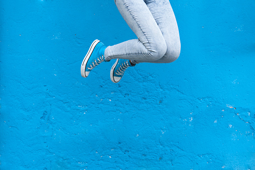 Jumping woman legs in blue sneakers against  blue wall background
