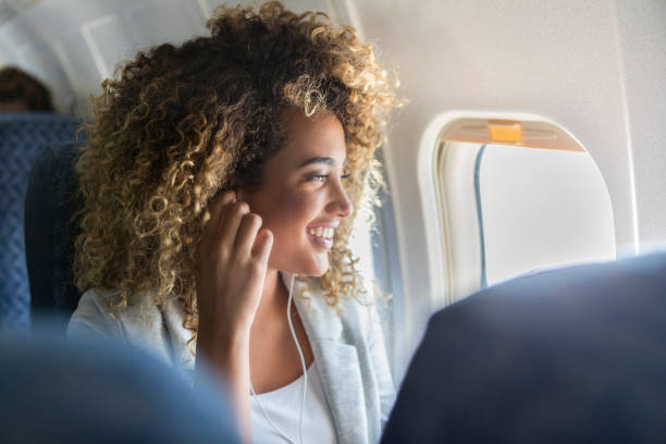 Woman listens to music during flight Attractive young woman wears earbuds to listen to music during a flight. She is sitting in a window seat gazing out of the window. plane window seat stock pictures, royalty-free photos & images