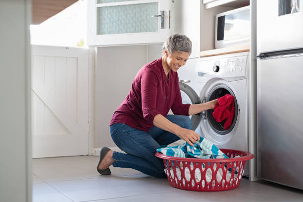 Woman loading clothes in washing machine Happy senior woman loading dirty clothes in washing machine. Smiling mature woman sitting on floor putting clothed in washing machine from laundry basket. Housework. dryer stock pictures, royalty-free photos & images