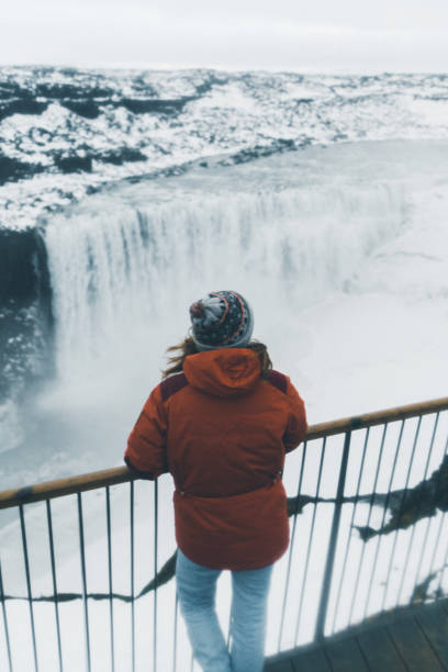 Woman looking at  Dettifoss waterfall in winter Young Caucasian woman  looking at  Dettifoss waterfall in winter dettifoss waterfall stock pictures, royalty-free photos & images