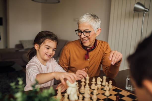 Woman looking at girl playing chess Happy mature woman teaching young girl play chess board game photos stock pictures, royalty-free photos & images