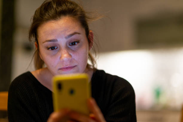 Woman looking at mobile phone screen feels confused at home at night time. stock photo