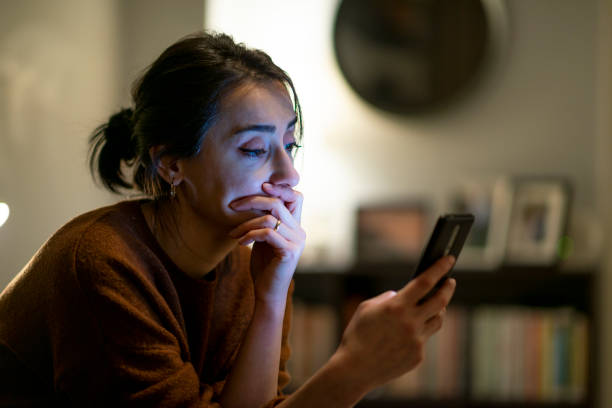 Woman looking at mobile phone screen feels upset at home at night time. stock photo