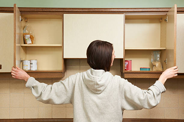 Woman Looking In Empty Food Cupboards Harsh economic times hitting household budgets cabinet stock pictures, royalty-free photos & images