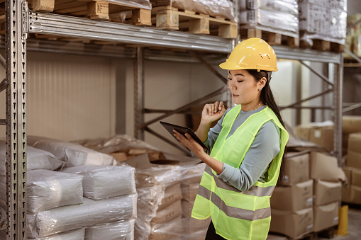 Asian woman worker working with digital tablet checking boxes Logistic import and export supplies packages in Warehouse , Logistics concept
