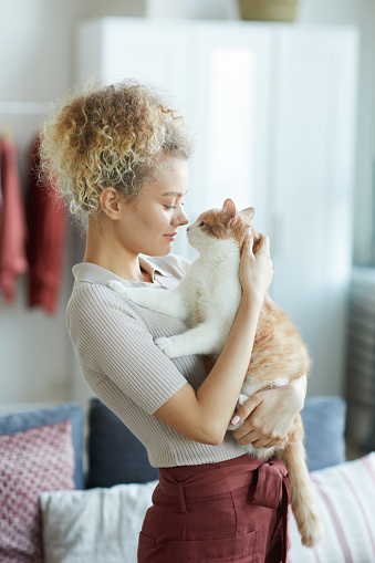 Young woman with curly hair standing and embracing her cute cat she loving it very much