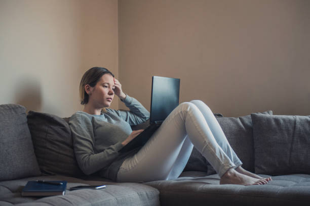 donna sdraiata sul divano e disperatamente alla ricerca di un lavoro sul suo laptop - kostic foto e immagini stock
