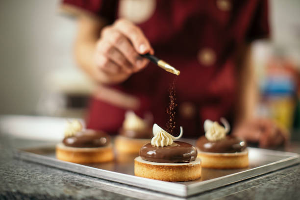 Woman making cakes in cake manufacture Mid adult woman decorating chocolate cookies with sweet powder on top. She works in sweet food manufacture, small business company chocolate photos stock pictures, royalty-free photos & images