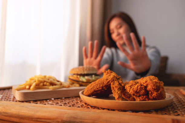 A woman making hand sign to refuse a hamburger, french fries and fried chicken on the table A woman making hand sign to refuse a hamburger, french fries and fried chicken on the table for dieting and healthy eating concept avoidance stock pictures, royalty-free photos & images