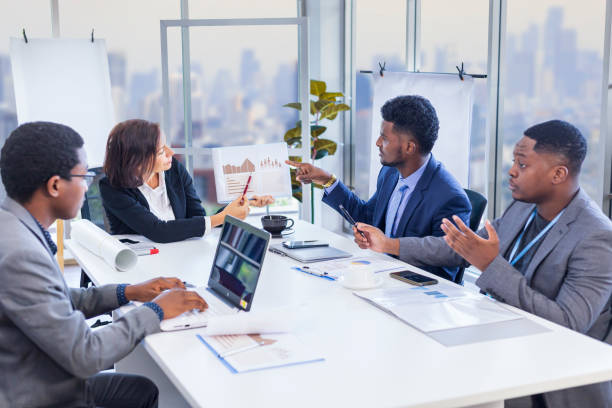 Woman manager is showing annual report chart to her African American colleagues in the executive meeting for next year plan with city skyline background for global business and investment concept stock photo