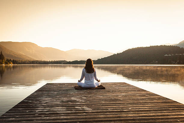 Woman meditating by lake. stock photo