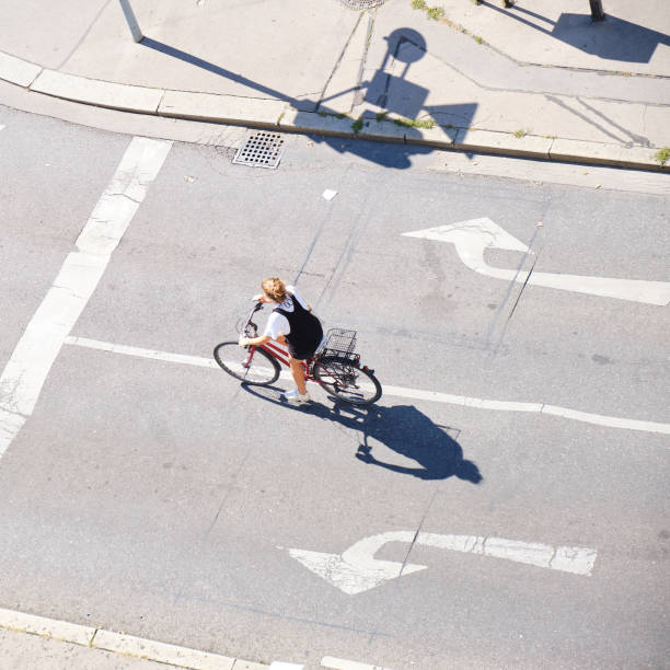 Woman on a bicycle, between left and right arrow signs - view from above with long shadows. stock photo