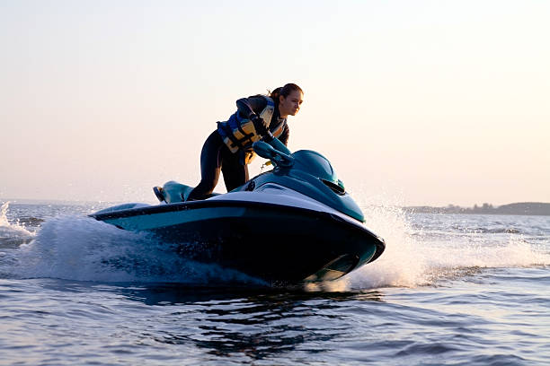Woman on a jet ski in the ocean during the sunset beautiful girl riding her jet skis in the sea at sunset. spray motorboat stock pictures, royalty-free photos & images