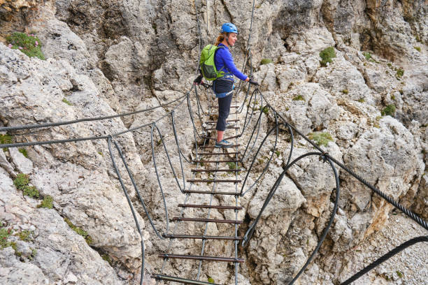 Woman on a via ferrata suspended wire bridge at Cesare Piazzetta klettersteig route, Sella group, Dolomites mountains, Italy. stock photo