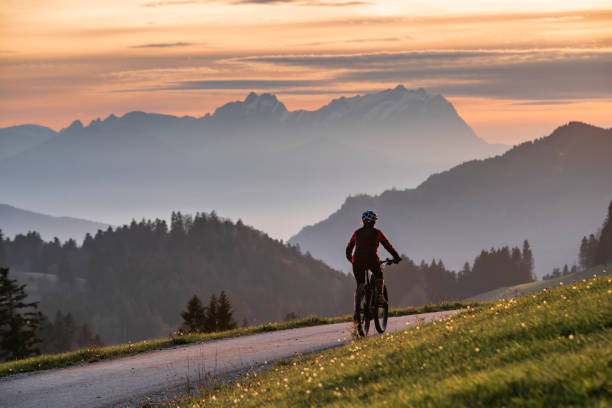 woman on electric mountain bike at sunset in swiss alps active woman riding her electric mountain bike at sunset in front of the awesome silhouette of Mount Saentis, Appenzell switzerland allgau alps stock pictures, royalty-free photos & images