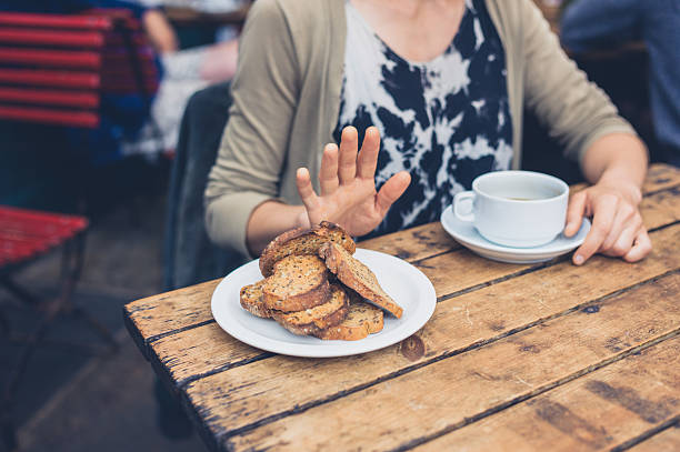 Woman on gluten free diet Young woman on gluten free diet is saying no thanks to toast in a cafe prejudice stock pictures, royalty-free photos & images