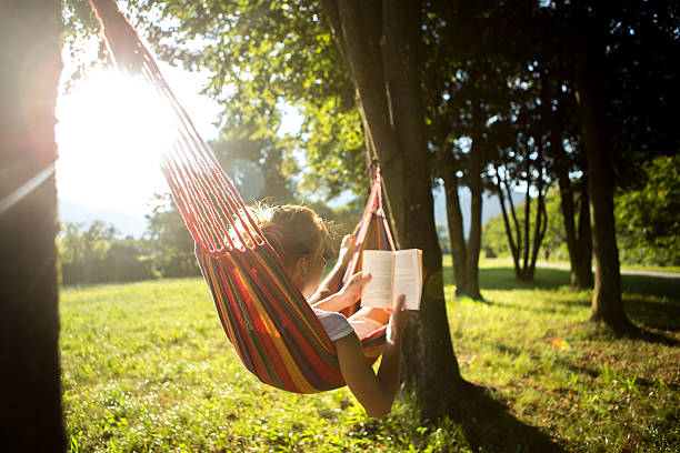 Woman on hammock at sunset reading book stock photo
