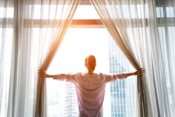 Woman opening curtains and looking out  waking up stock pictures, royalty-free photos & images