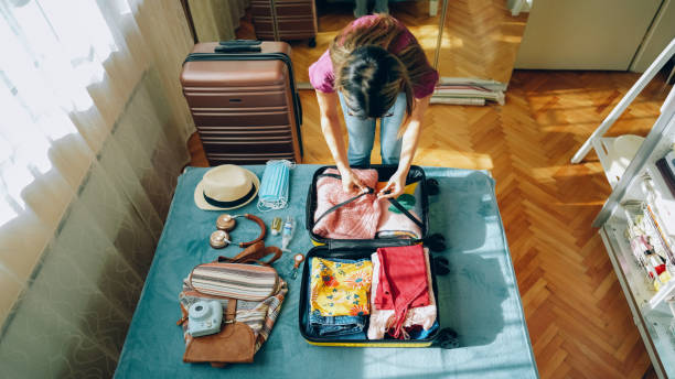 Woman packing suitcase for travel Woman packing suitcase for summer travel, including face masks and airplane travel-sized antibacterial hand gels light luggage stock pictures, royalty-free photos & images