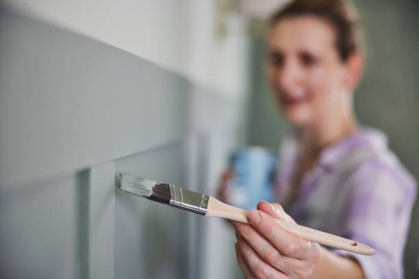 Woman Painting Wall With Panelling In Room Of House With Paint Brush stock photo