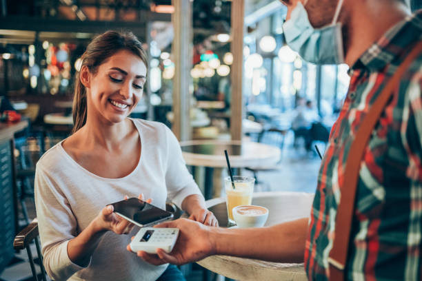 Woman paying contactless with smart phone at the restaurant. Beautiful young woman using smartphone for paying to the waiter in a restaurant. approaching stock pictures, royalty-free photos & images
