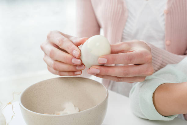 Woman peeling boiled egg Close-up partial view of young woman peeling boiled egg boiled egg stock pictures, royalty-free photos & images