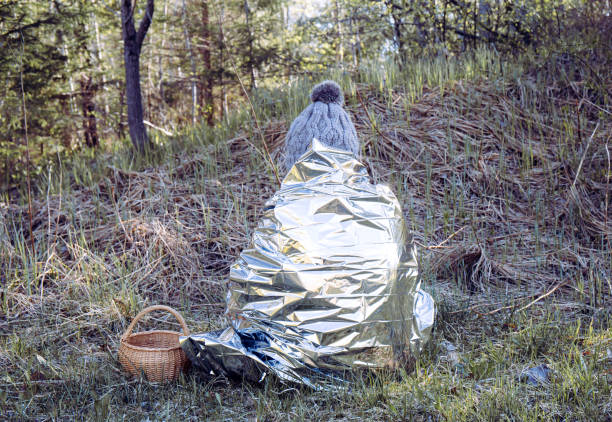 woman person is lost and sit in wild forest in cold day, using first aid emergency blanket to prevent hypothermia and body heat loss. emergency blanket concept. - lost first imagens e fotografias de stock