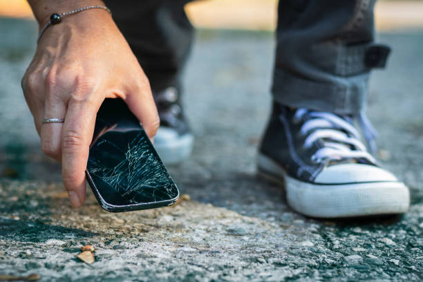 Woman picking up broken smartphone from the ground. Damaged mobile phone with cracked touch screen. broken stock pictures, royalty-free photos & images