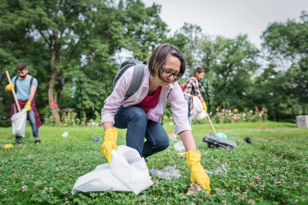 Woman picking up litter in the park Group of volunteers in the park cleaning up and gathering trash in garbage bags environmental consciousness stock pictures, royalty-free photos & images