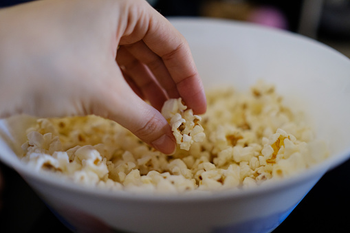 Woman picking up popcorn from a bowl watching a movie at home