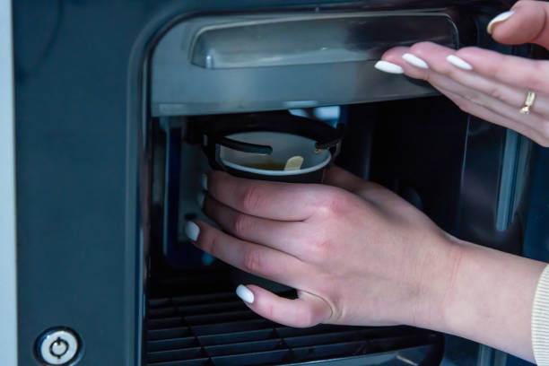 frau holt kaffee vom automaten ab - kaffeeautomat stock-fotos und bilder