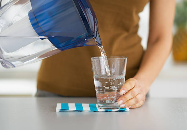 Woman pouring a glass of water from a filter jug Closeup on housewife pouring water into glass from water filter pitcher jug stock pictures, royalty-free photos & images
