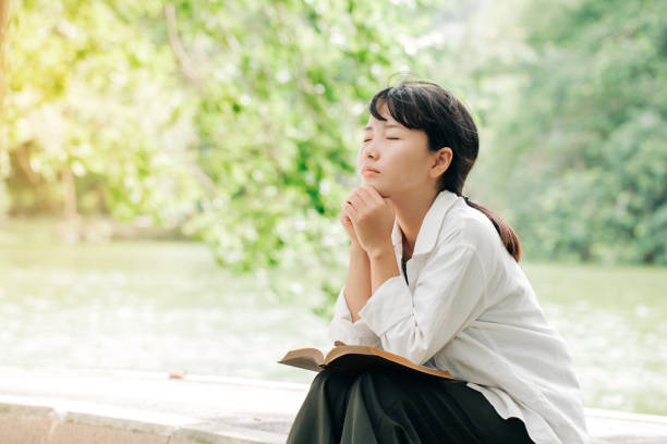 Woman praying in the morning on nature background.Hands folded in prayer on a Holy Bible in church concept for faith, spirituality and religion Woman praying in the morning on nature background.Hands folded in prayer on a Holy Bible in church concept for faith, spirituality and religion praying stock pictures, royalty-free photos & images