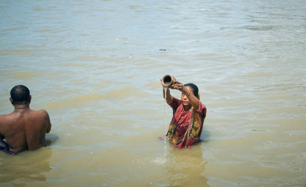 A woman praying to God in Ganges water, on the day of Mahalaya Mallick Ghat, Kolkata, 09/17/2020: A Hindu woman doing the "Tarpan" ritual, standing in Ganges water near ghat. She is pouring water from a pot and looking towards sun, which is an act of offering. Tarpan is generally held in Pitru Paksha, which is is fortnight-long Hindu ritual marked annually, to pay homage to departed souls and ancestors. offering water to sun stock pictures, royalty-free photos & images