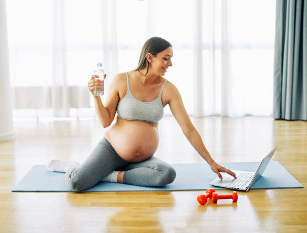 woman pregnant mother pregnancy female exercise sport fitness belly healthy maternity motherhood health yoga young dumbbell weight laptop computer online water drink bottle hydrate stock photo