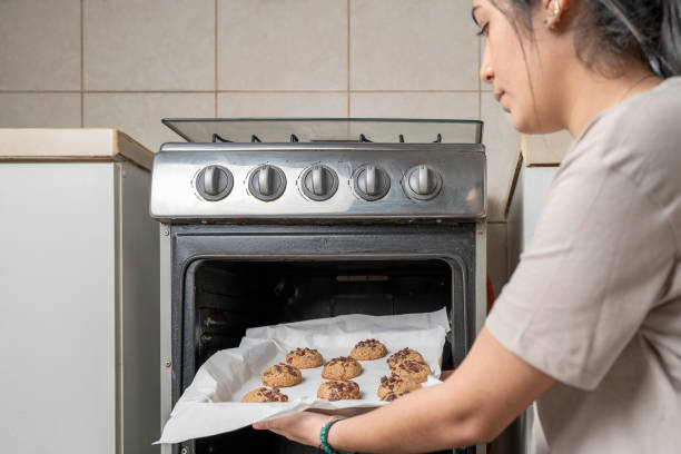 Woman pulling a plate of healthy biscuits out of a oven Middle-aged latina woman pulling a plate of healthy biscuits out of a oven at home hot peruvian women stock pictures, royalty-free photos & images