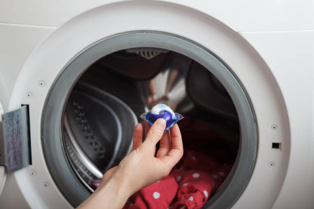 Woman putting detergent pod in washing machine with laundry, closeup stock photo