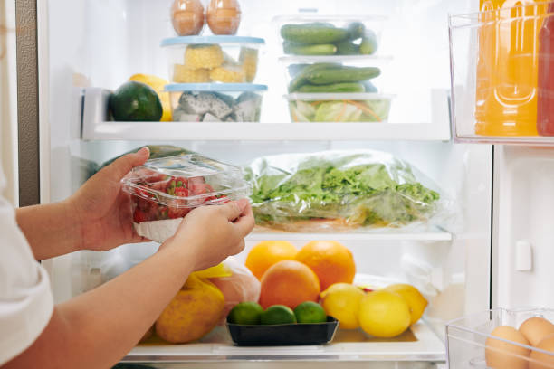 frau legt erdbeeren in kühlschrank - kühlschrank stock-fotos und bilder