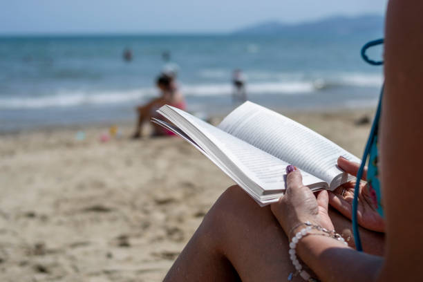 Woman reading a book on the beach, blurred background. Summer leisure on the beach stock photo