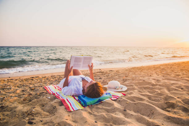 woman reading a book on the beach - beach towel imagens e fotografias de stock