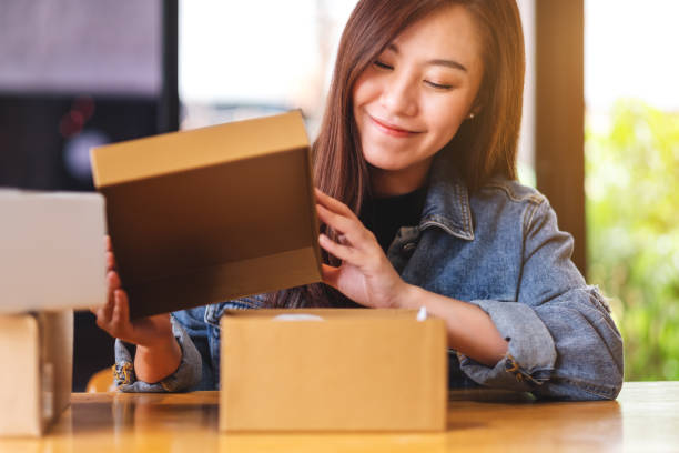 een vrouw die een postpakketdoos bij huis voor levering en online het winkelen concept ontvangt en opent - unbox stockfoto's en -beelden