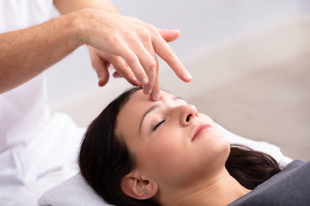 Woman Receiving Reiki Treatment Close-up Of A Young Woman Receiving Reiki Treatment By Therapist alternative medicine stock pictures, royalty-free photos & images