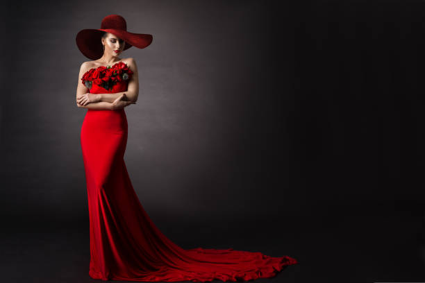 Woman red Dress and Hat. Fashion Model in Long evening Gown with Flowers. Black Studio Background stock photo