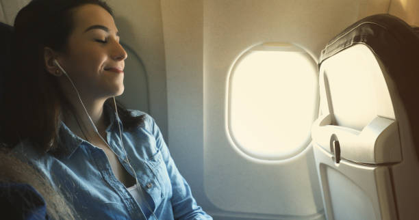 Woman relaxes while flight on commercial airplane Beautiful young Caucasian woman closes her eyes while listening to music while on a commercial flight. plane window seat stock pictures, royalty-free photos & images