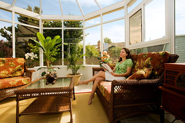 Woman Relaxing in Cozy Conservatory Photo of a young woman sitting in a cozy solarium with a magazine. greenhouse table stock pictures, royalty-free photos & images