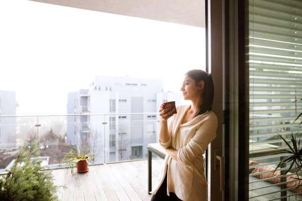 Woman relaxing on balcony holding cup of coffee or tea Beautiful young woman relaxing on balcony with city view holding cup of coffee or tea balcony stock pictures, royalty-free photos & images