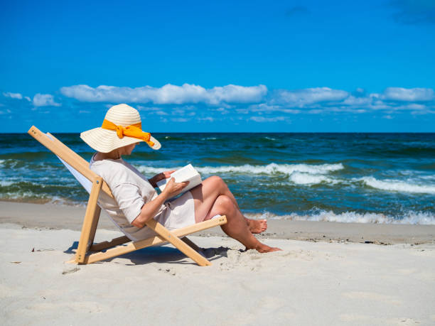 Woman relaxing on beach reading book stock photo