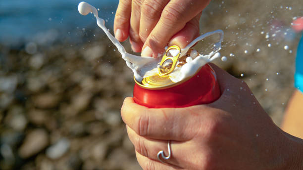 MACRO: Woman relaxing on the beach opens up a can of beer and gets sprayed. stock photo
