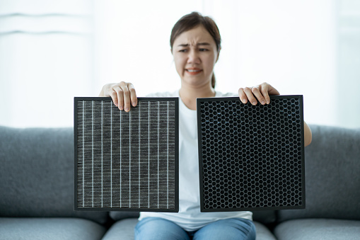 Beautiful Asian young woman holding a HEPA carbon air purifier filter in living room, woman prepare a air purifier filter to be replace the old one. Healthcare and good living lifestyle concept.