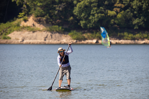 A Japanese woman rides her stand up paddle board on a calm lake on a sunny day.